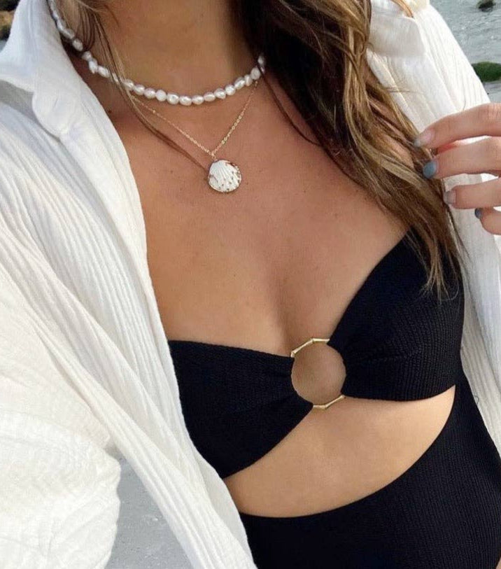 Person wearing a black bikini top with a gold circle design, white shirt, and seashell necklace with a gold chain.