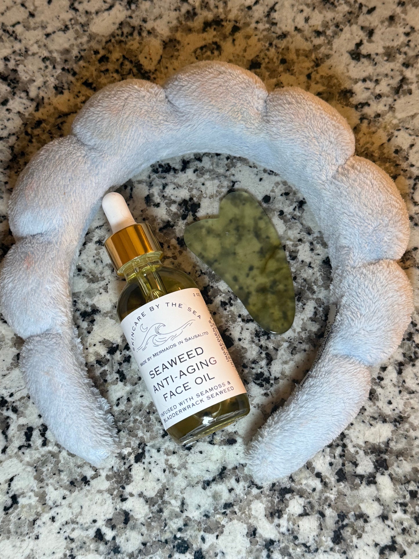 Flatlay of seaweed anti-aging face oil with guasha and headband to show skincare routine