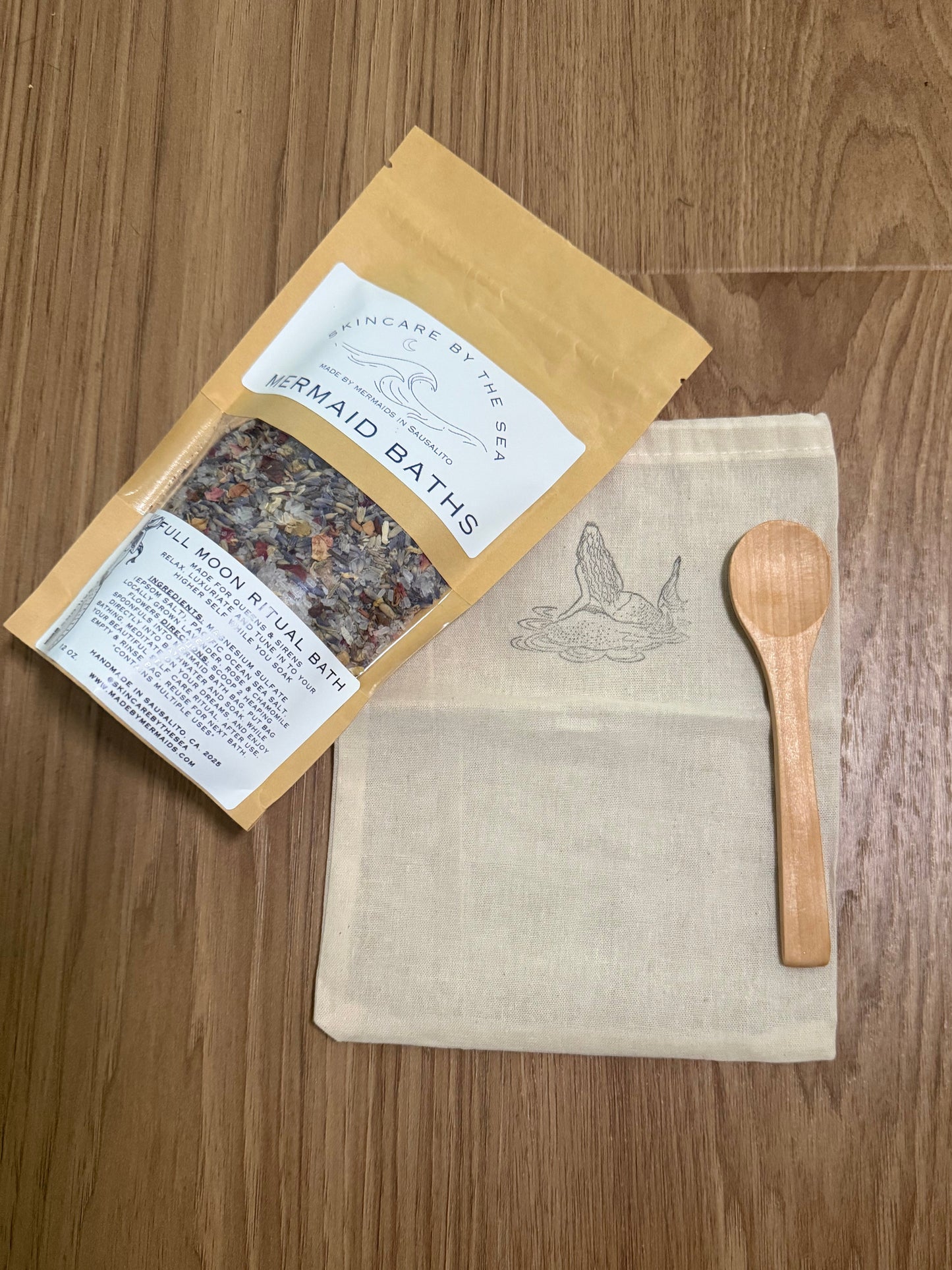 Herbal bath package with a wooden spoon and pouch for bath salts on a wooden surface