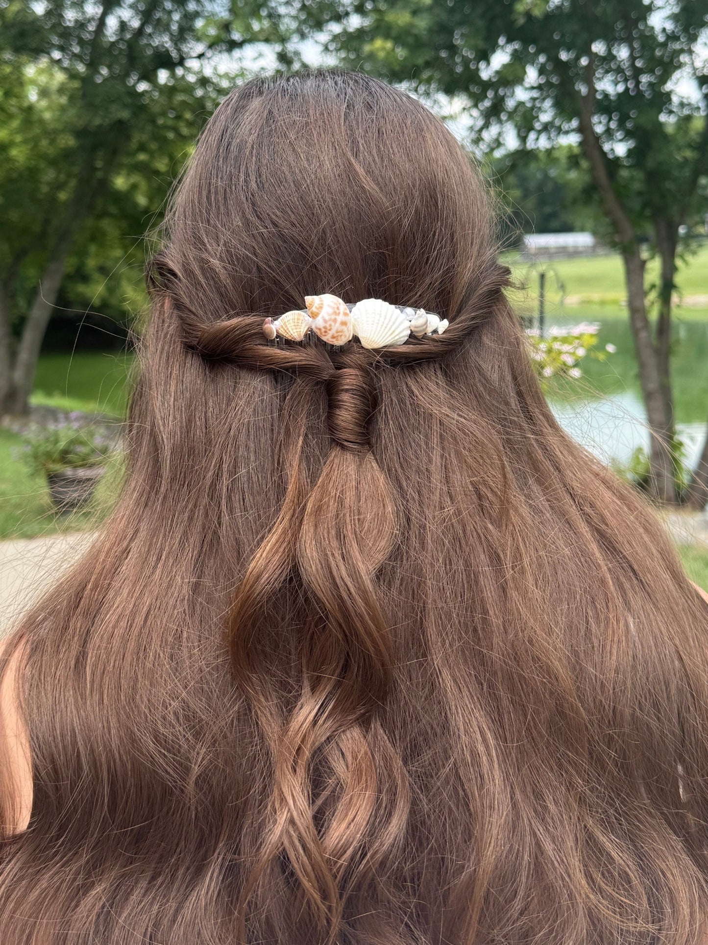 Person with long, wavy hair wearing a seashell hair comb accessory outdoors.