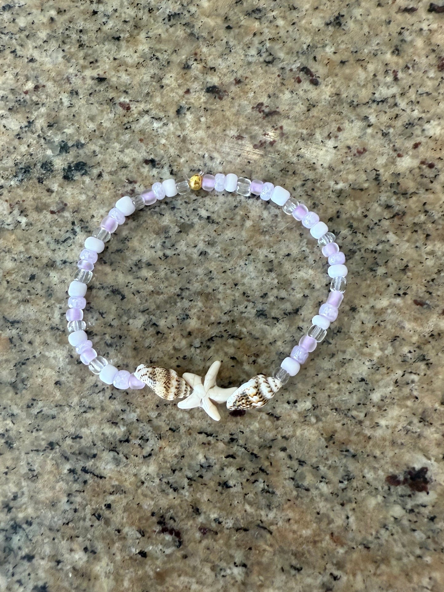 Beaded bracelet with a starfish charm and seashells on a textured surface