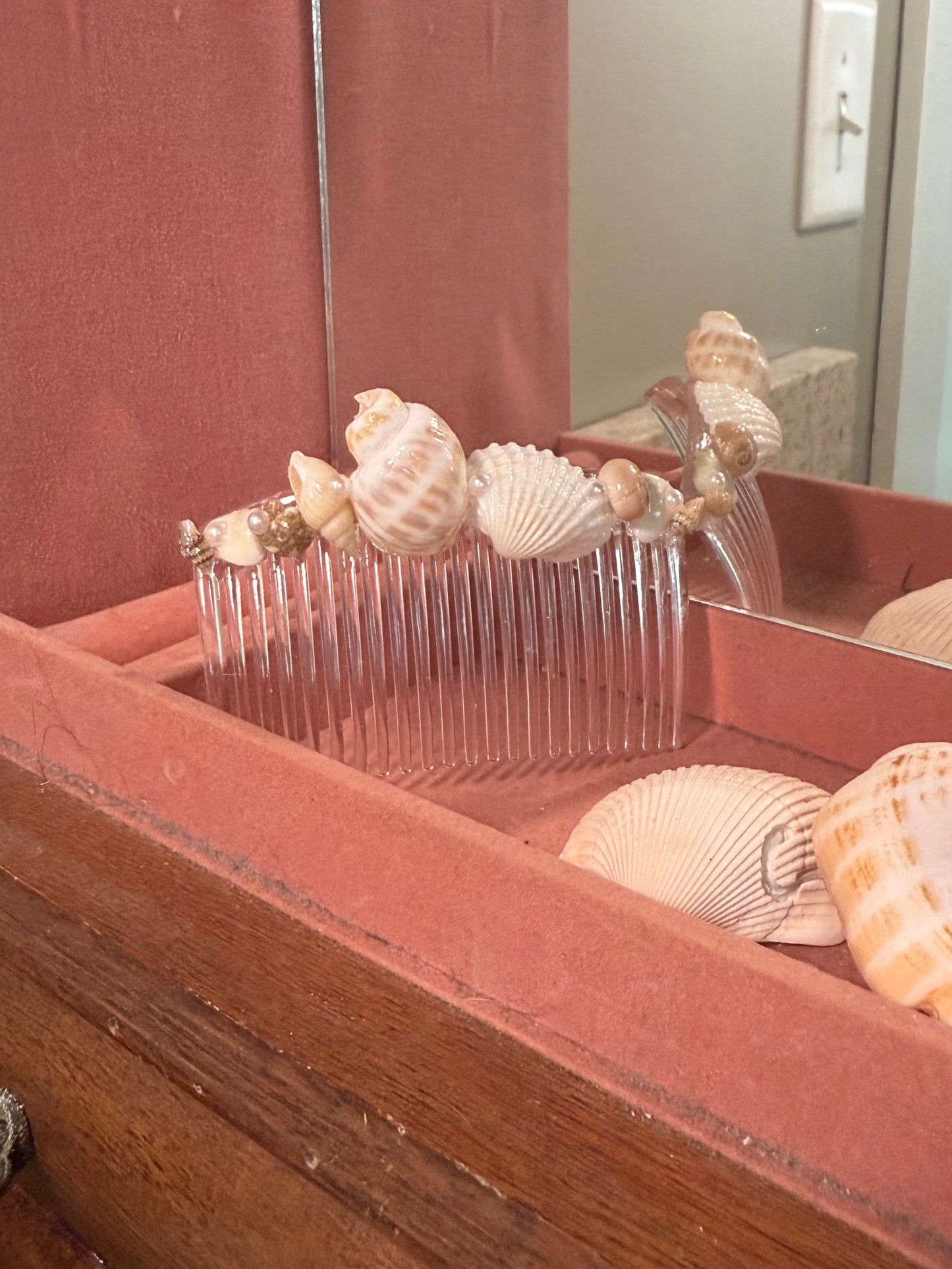 Wooden cabinet with seashell hair comb inside, reflected on a mirror.