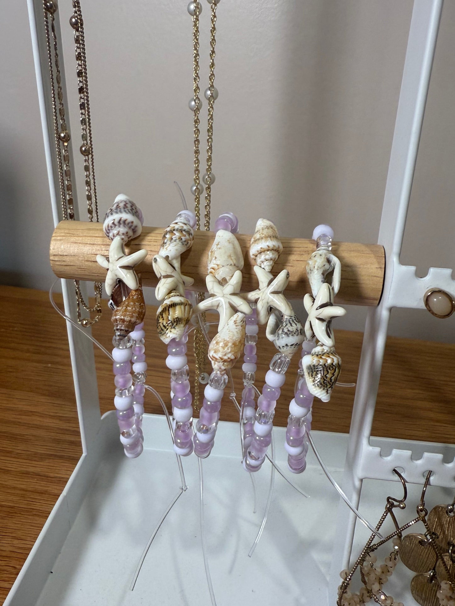 Bracelets displayed with necklaces on a wooden stand against a white background