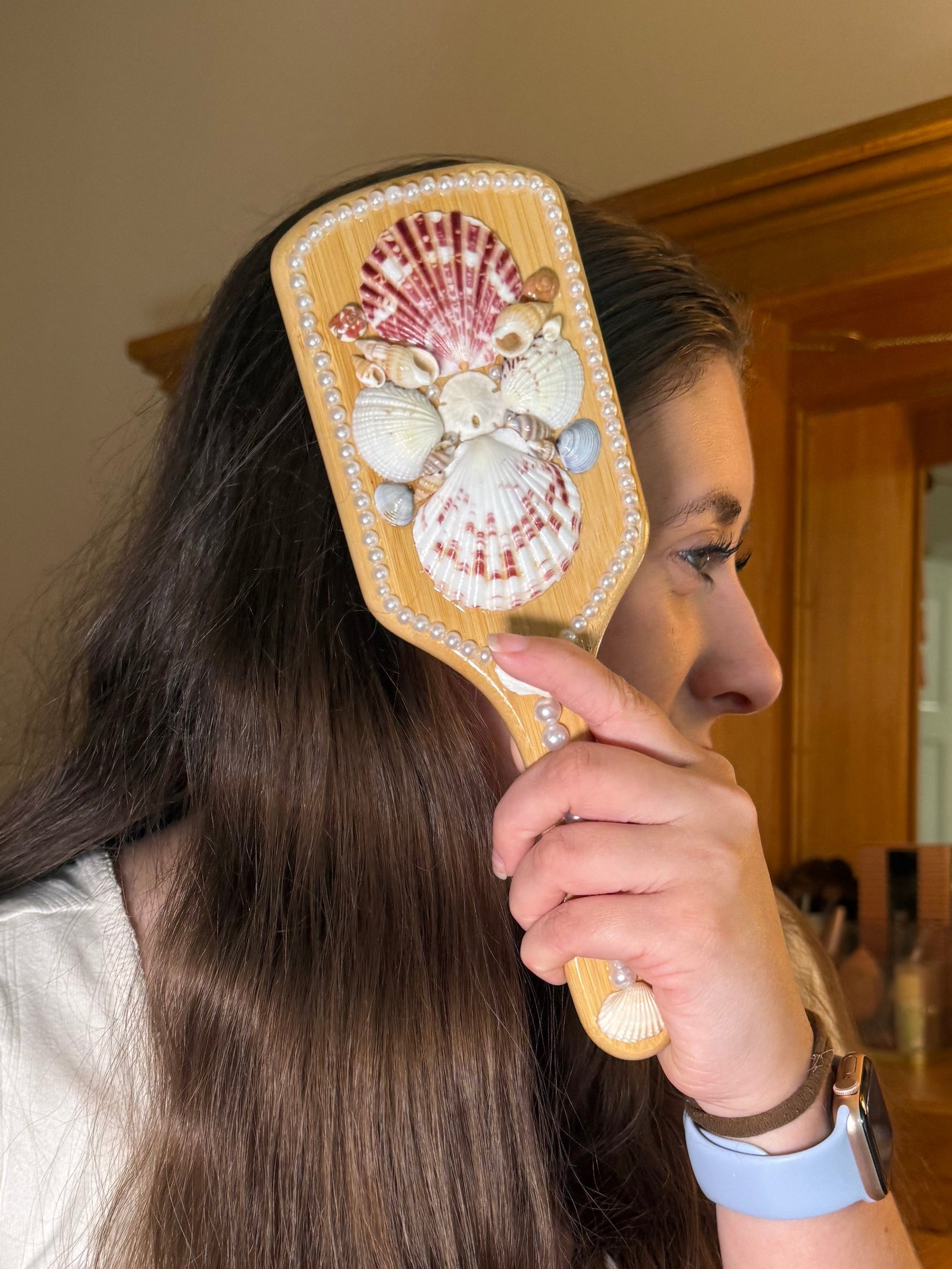 Person brushing their hair with a decorative hair brush in a bathroom setting