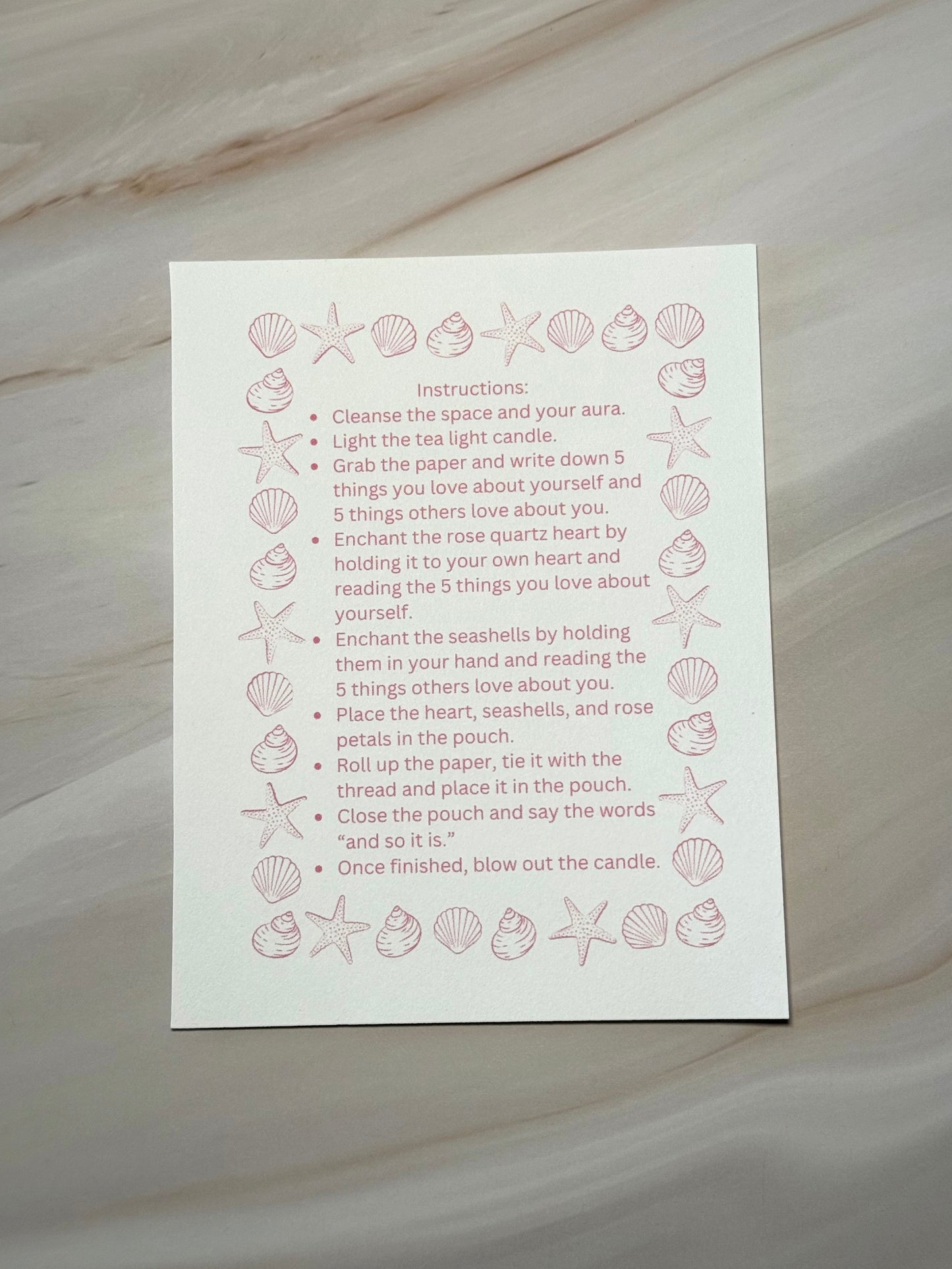 White card with instructions with pink shell designs and text on a marble surface