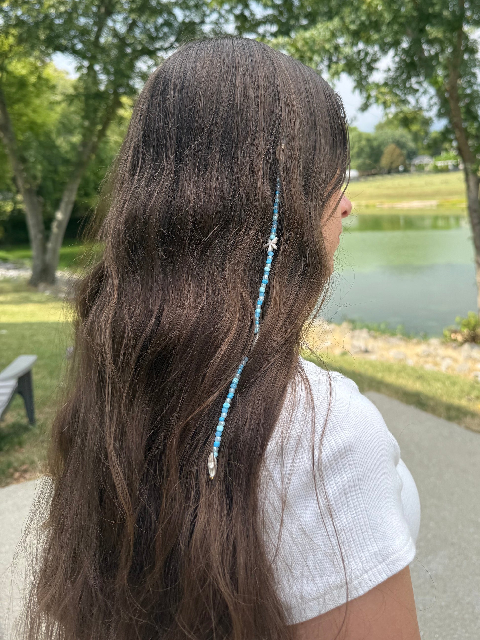 Person with long hair wearing a blue hair extension clip accessory in a park setting