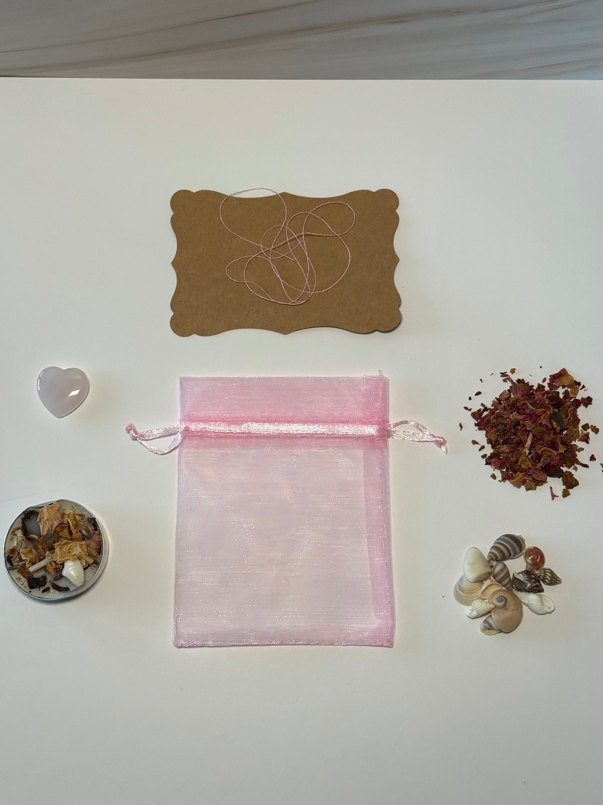 Pink drawstring bag with dried herbs and a small heart-shaped object on a white surface.