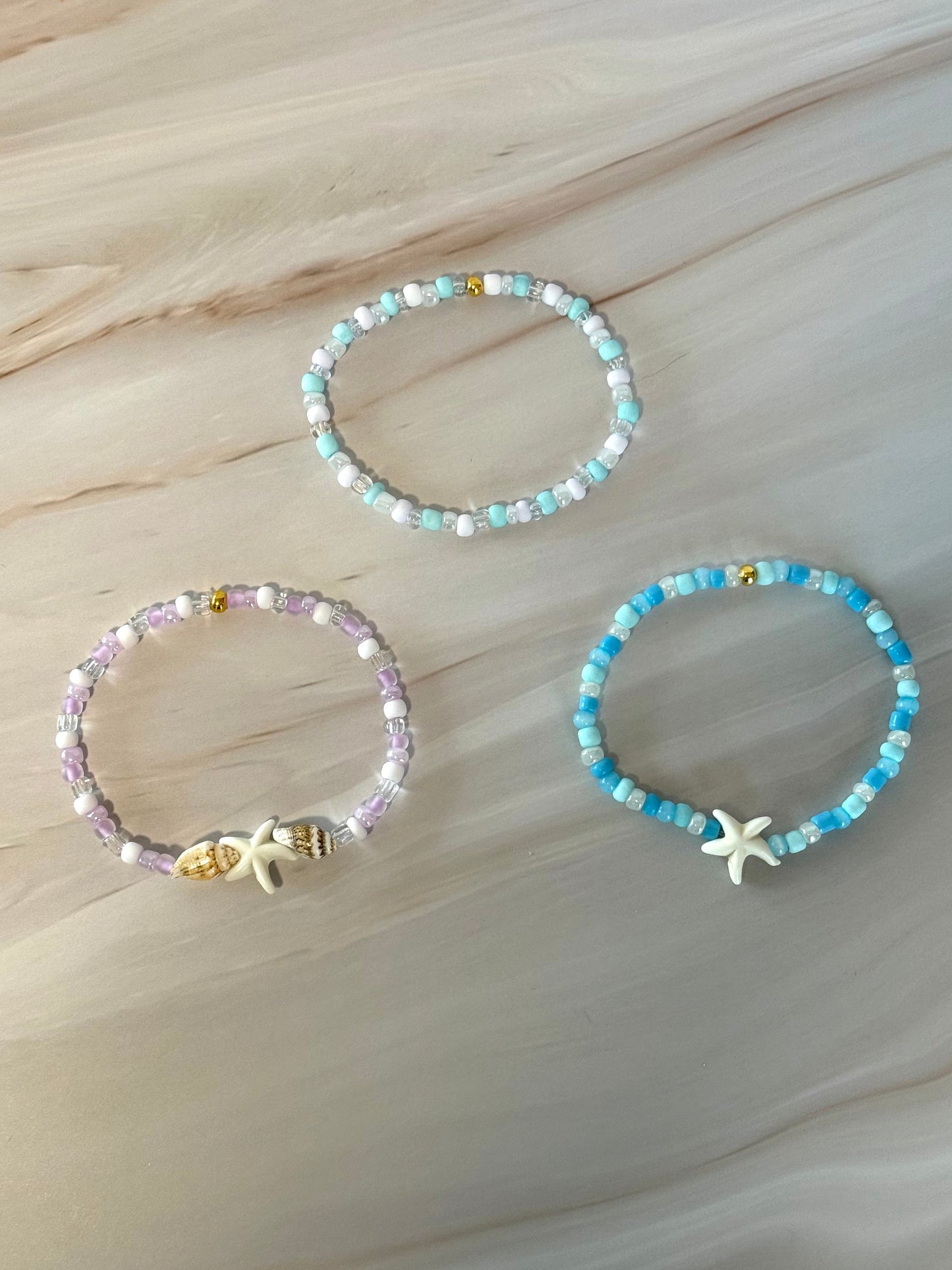 Three beaded bracelets with starfish charms on a marble surface