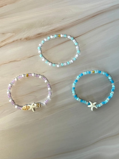 Three beaded bracelets with starfish charms on a marble surface