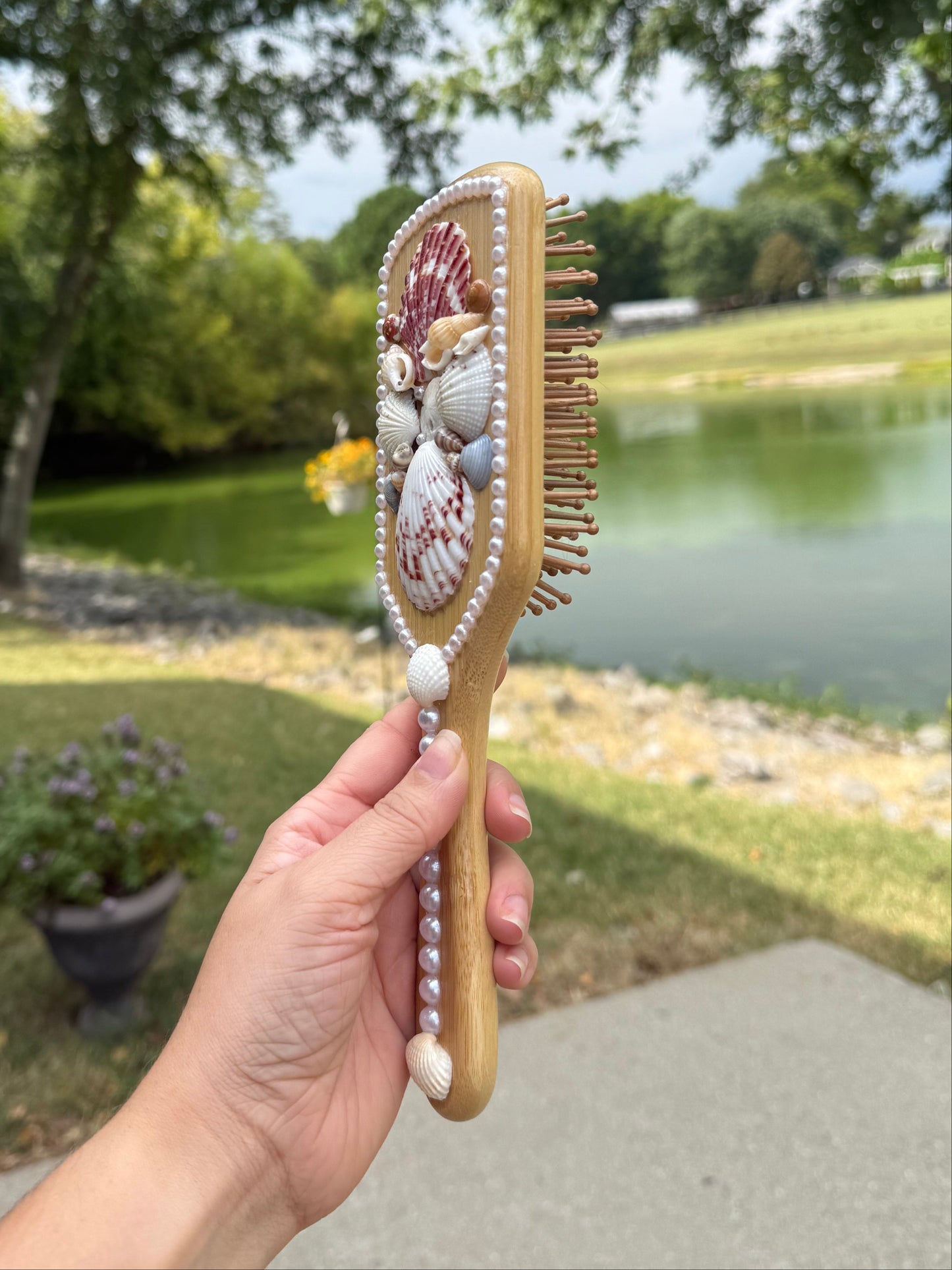 Hand holding a decorative hairbrush with a blurred outdoor background