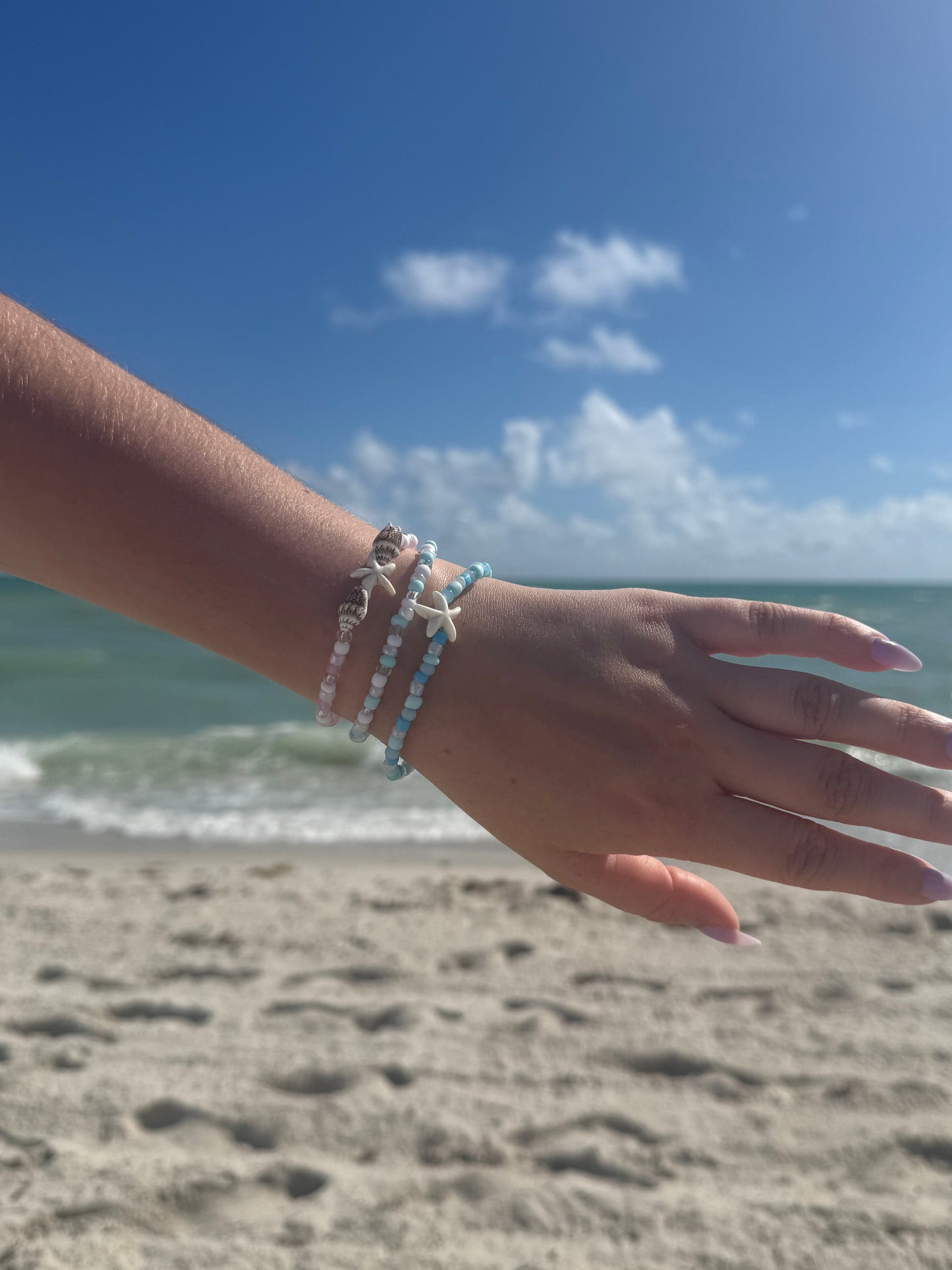 Hand with a seashell bracelets against a blue sky and ocean backdrop