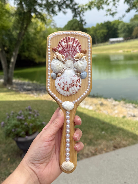 Hand holding a decorative shell hairbrush with a park in the background