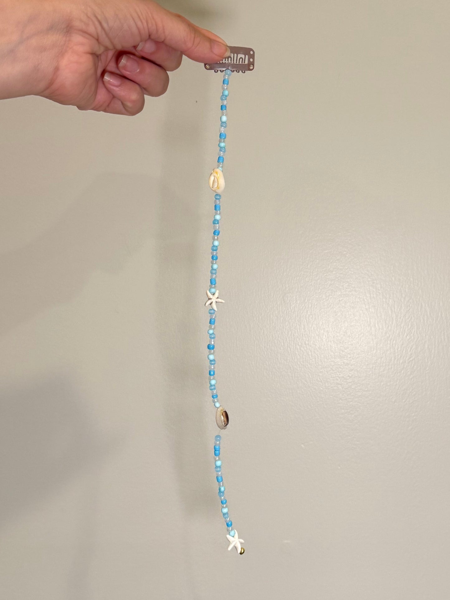 Hand holding a beaded seashell hair extension clip with decorative elements against a neutral background