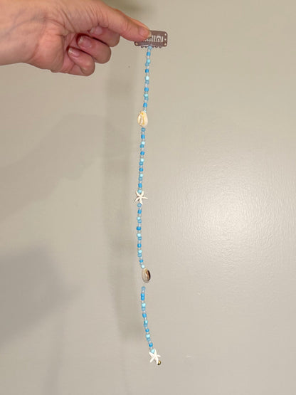 Hand holding a beaded seashell hair extension clip with decorative elements against a neutral background