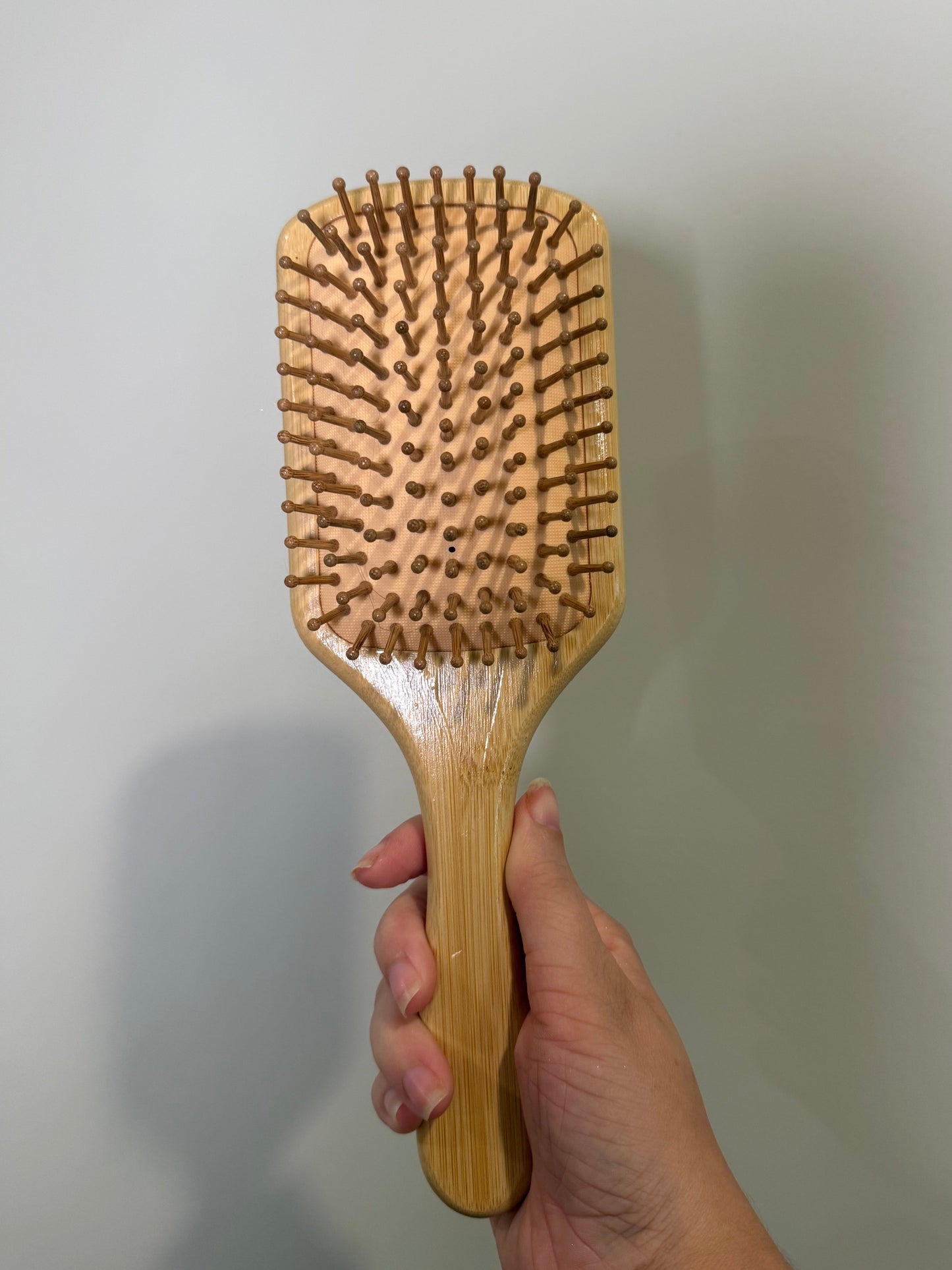 Wooden hairbrush held by a hand against a plain background