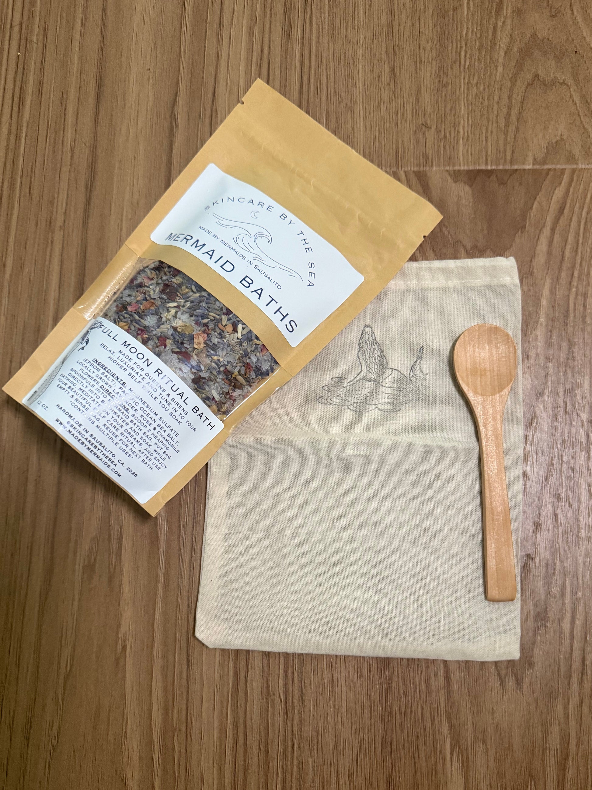 Herbal bath package with a wooden spoon and pouch for bath salts on a wooden surface