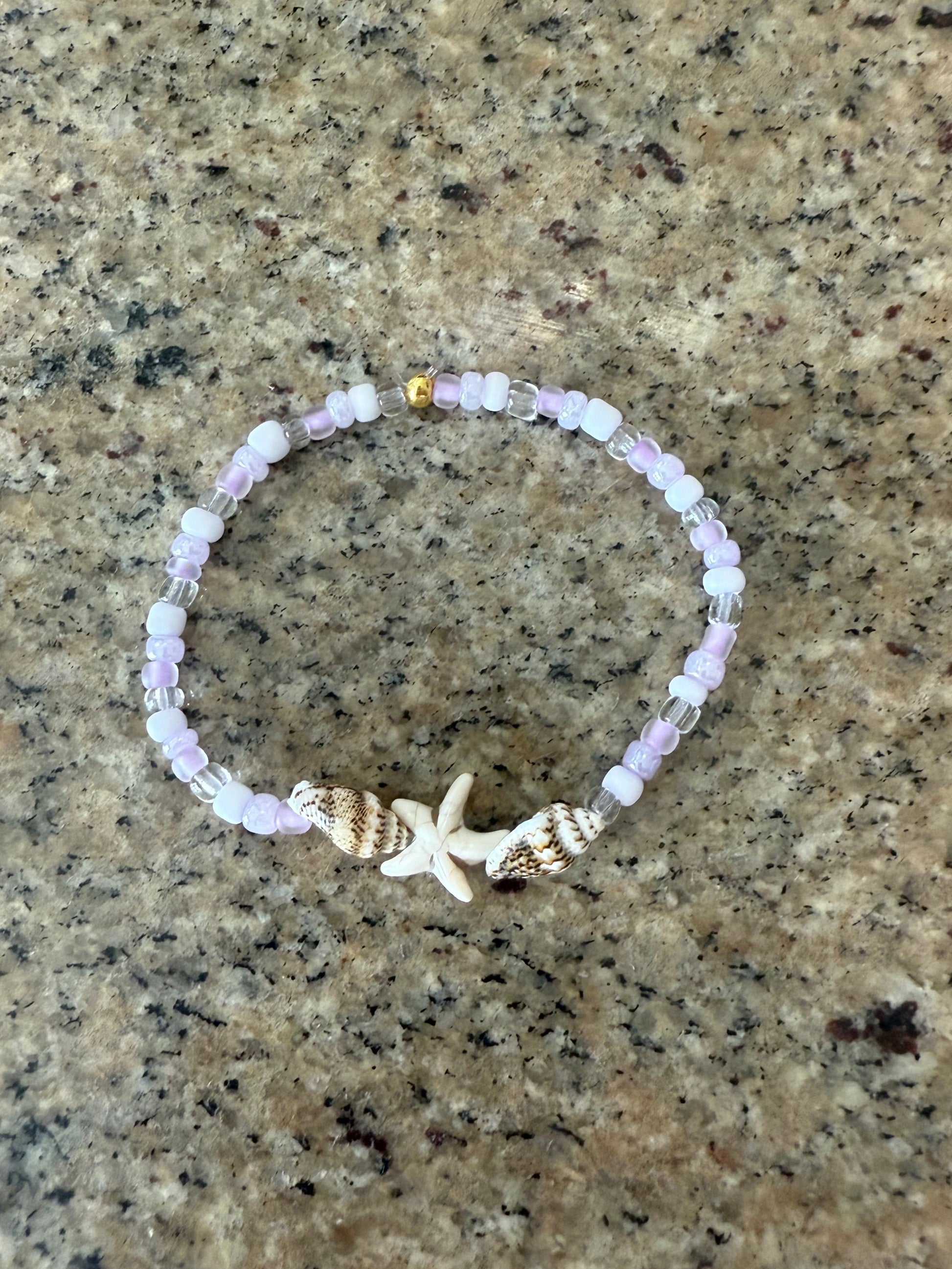 Beaded bracelet with a starfish charm and seashells on a textured surface