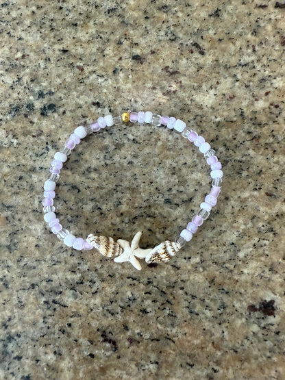 Beaded bracelet with a starfish charm and seashells on a textured surface