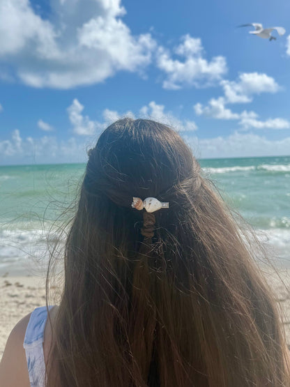 Person with a hair clip on a beach with ocean and sky in the background