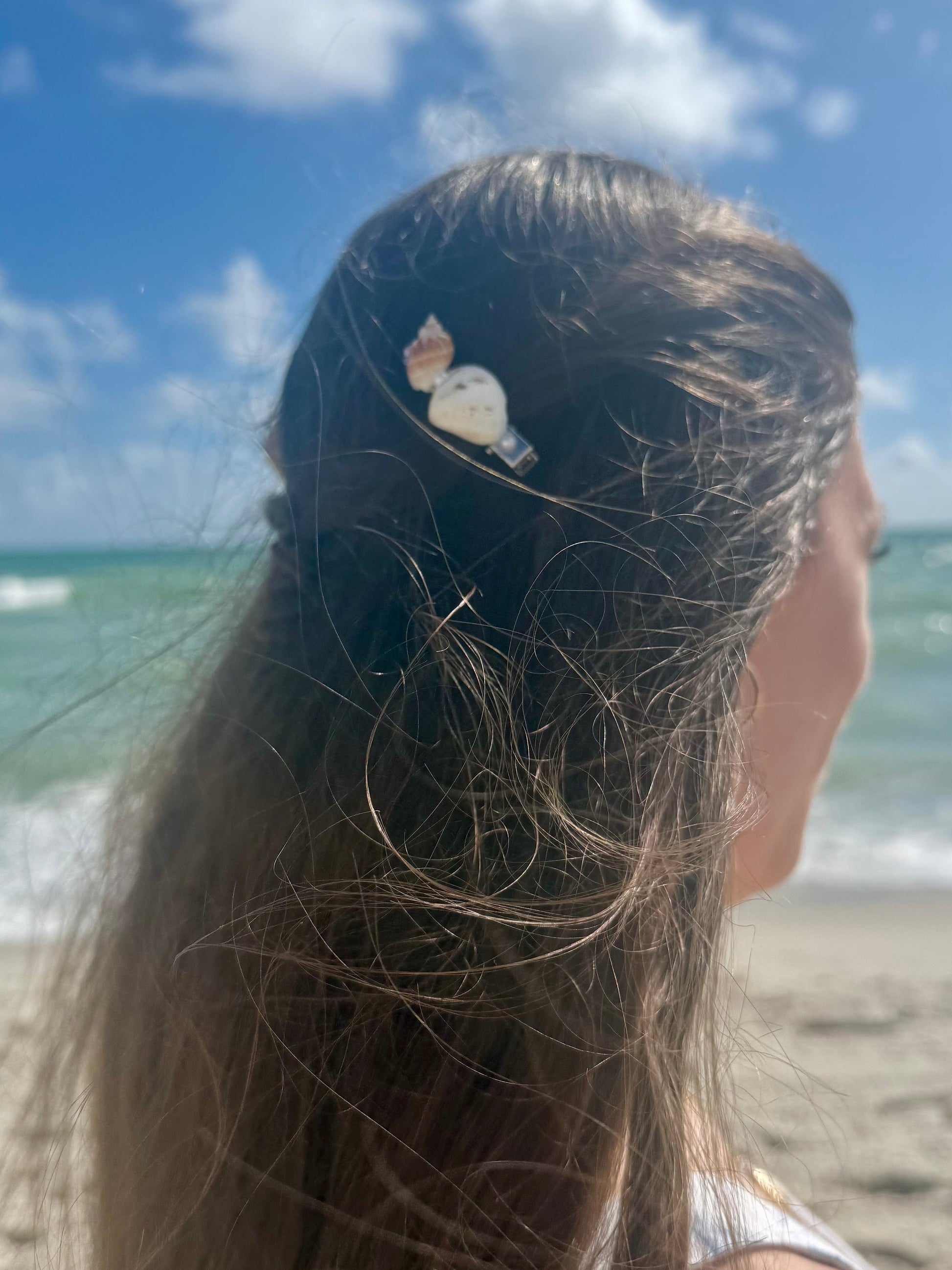 seashell hair clip in woman's hair with beach ocean sky background