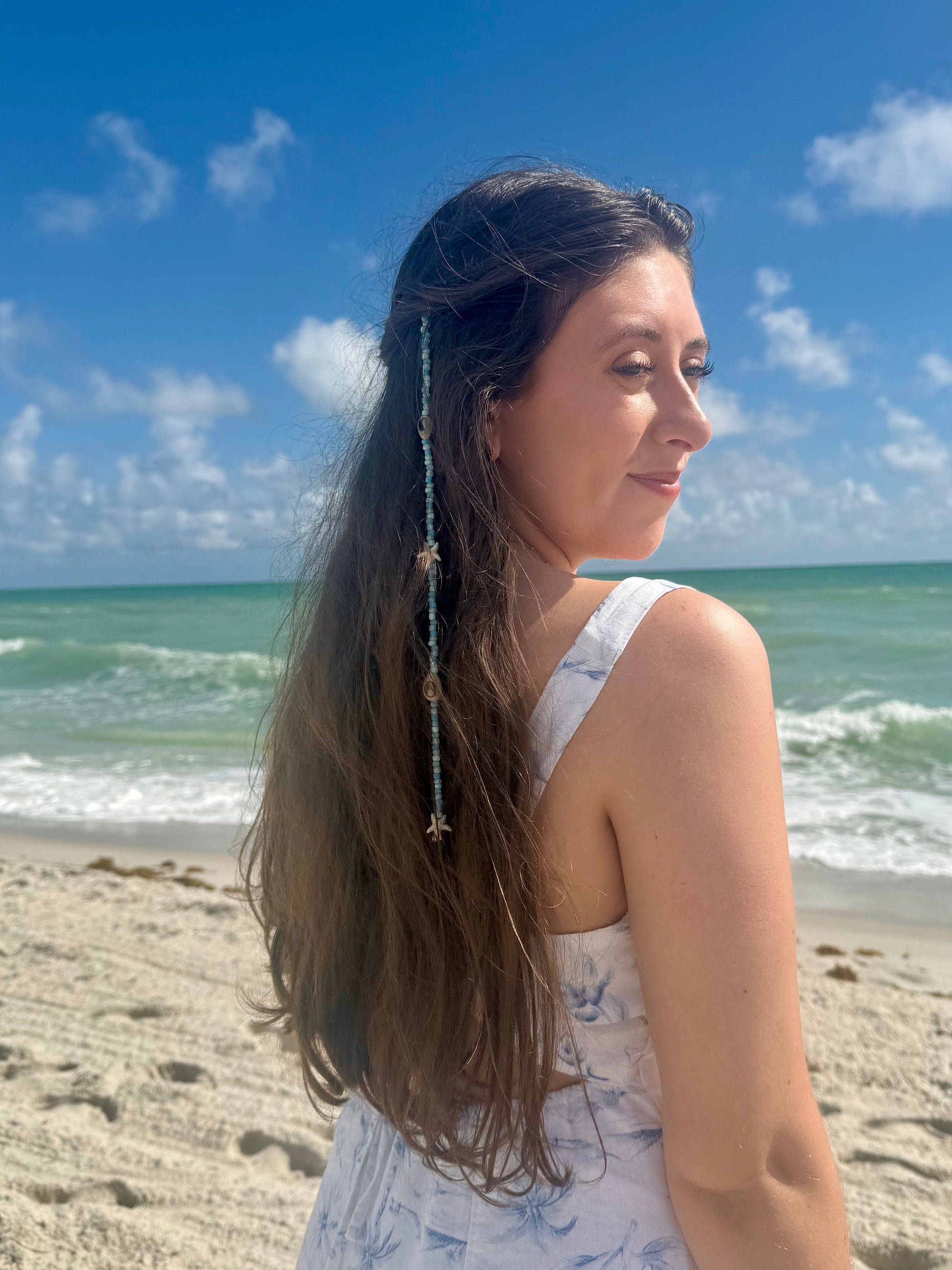 Woman on a beach with ocean and blue sky in the background wearing seashell hair extension clip in her hair