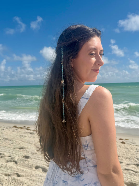 Woman on a beach with ocean and blue sky in the background wearing seashell hair extension clip in her hair