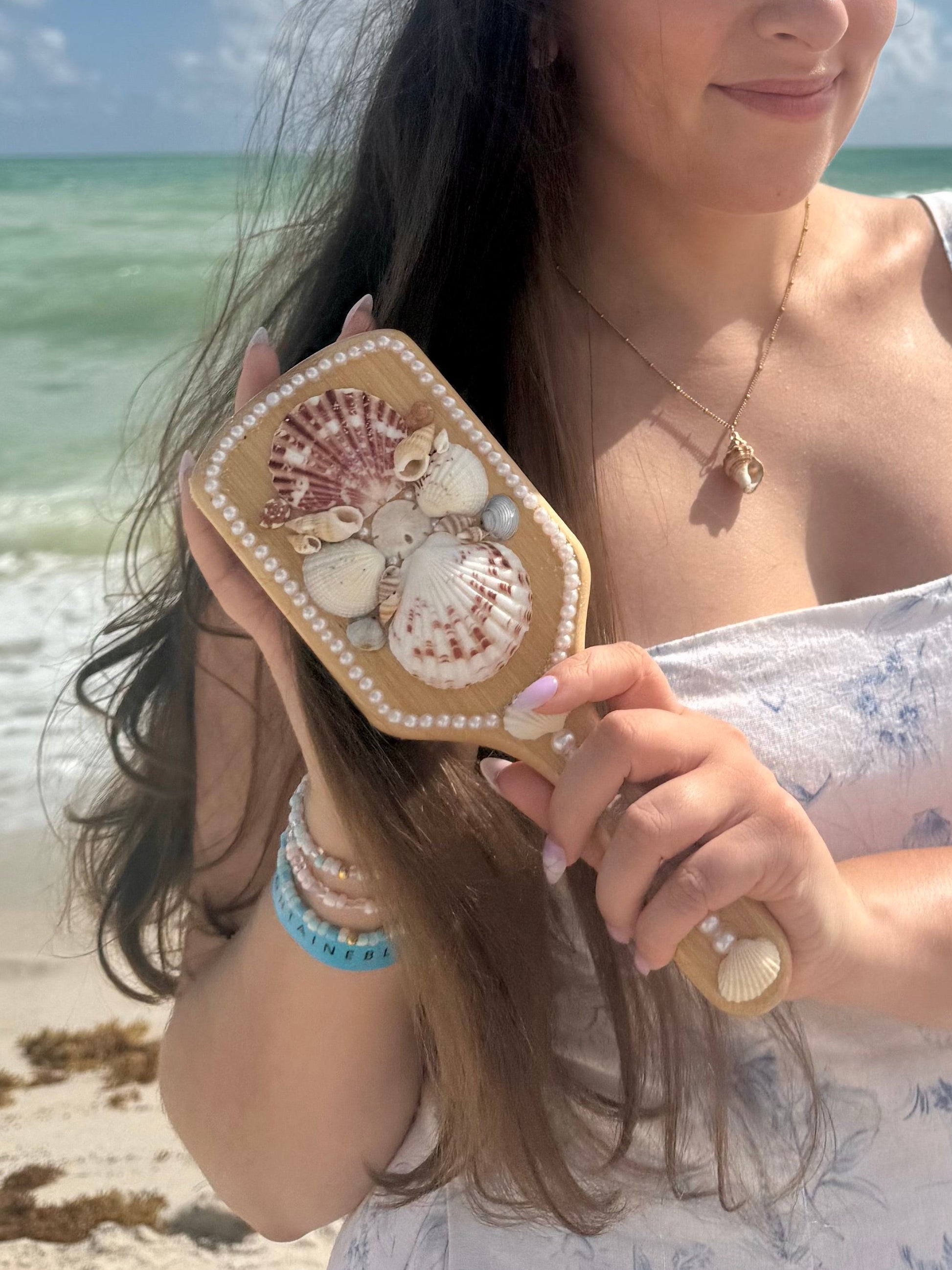 woman brushing her hair on the beach with seashell hairbrush