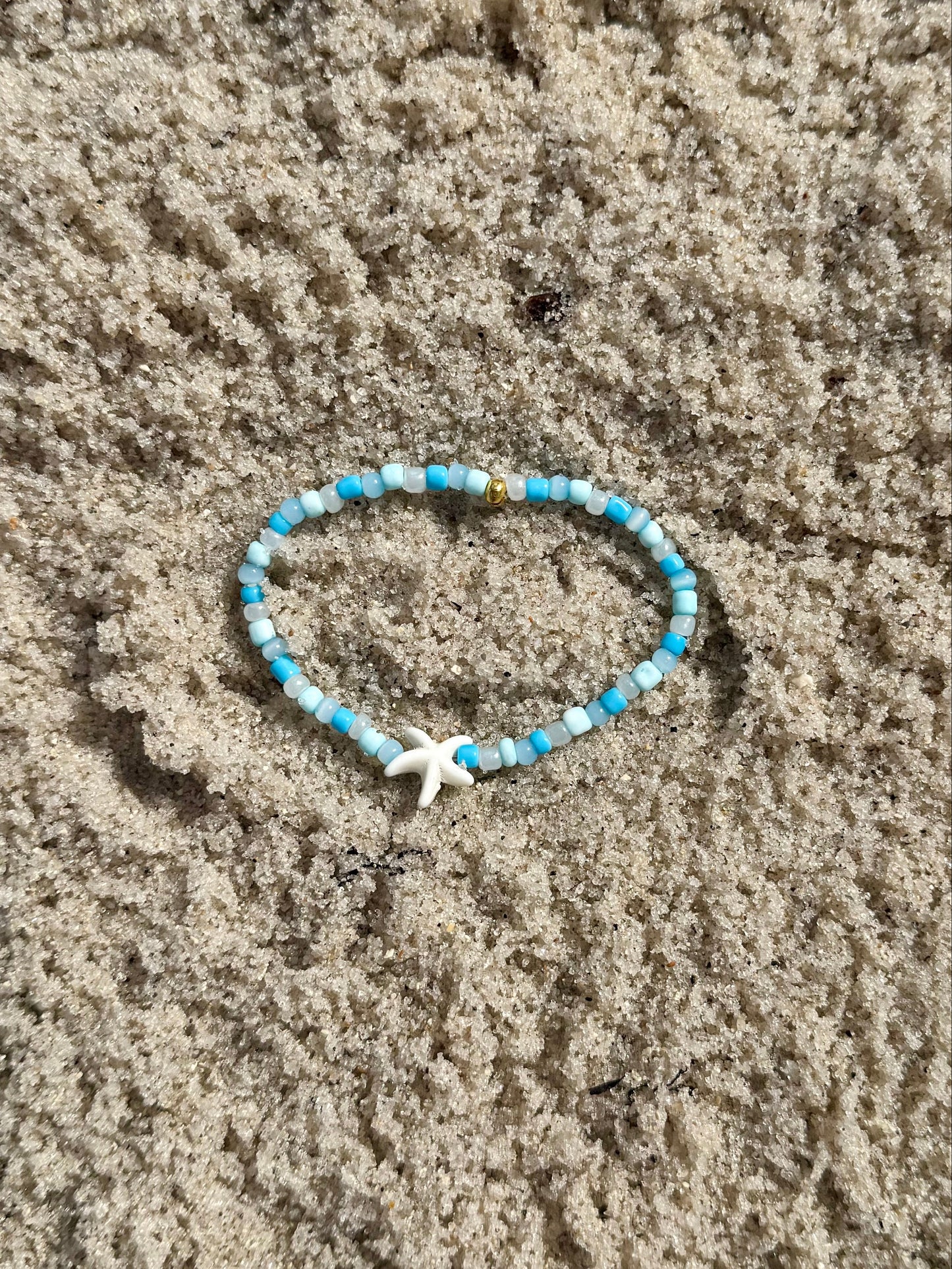 Blue beaded bracelet with a starfish charm on sandy ground