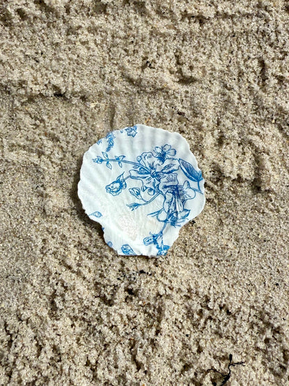 Blue and white floral-patterned seashell on sandy ground