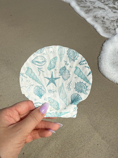 Hand holding seashell trinket dish with sand and water background
