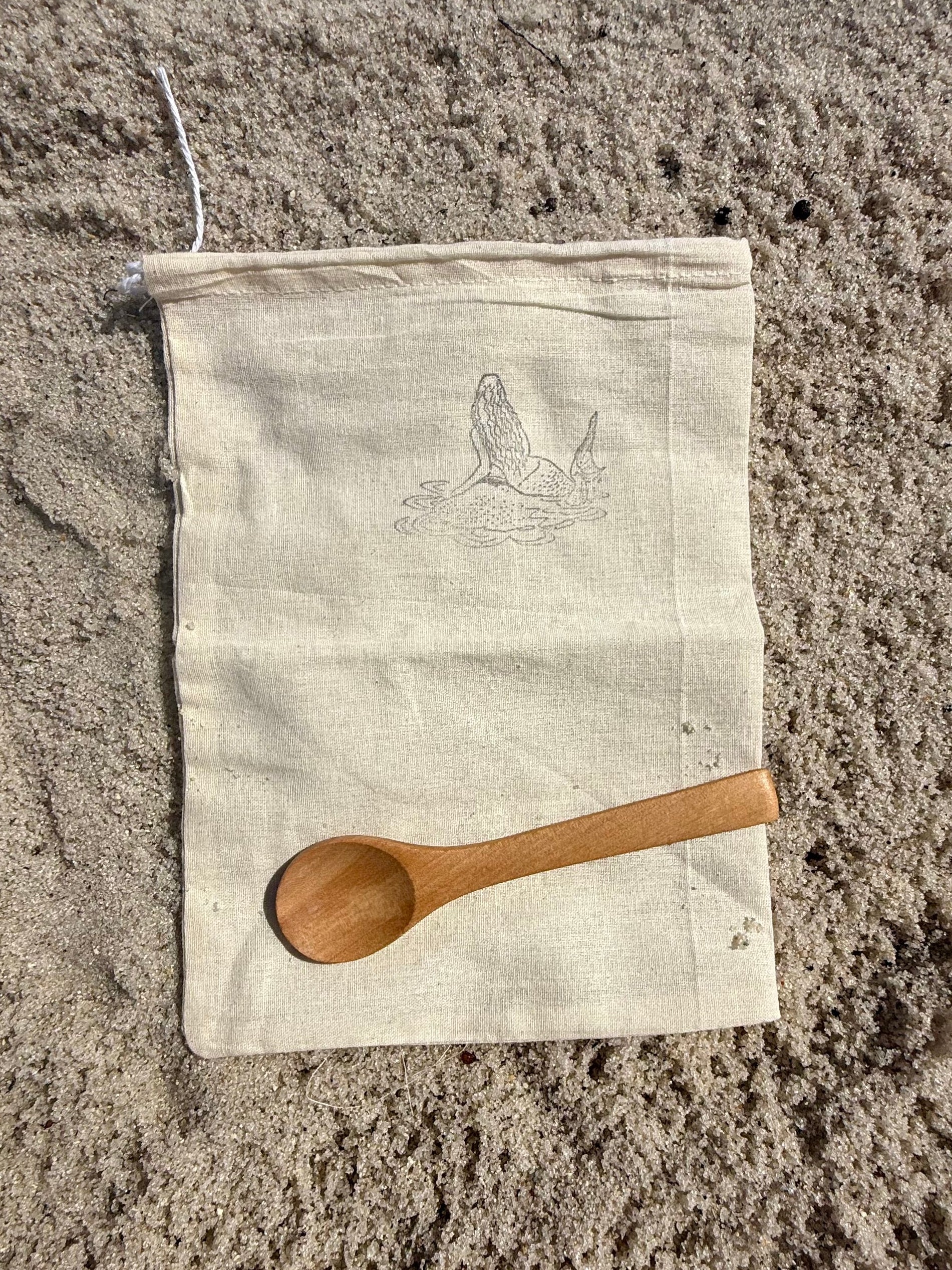 Wooden spoon on a white cloth bag on sandy ground