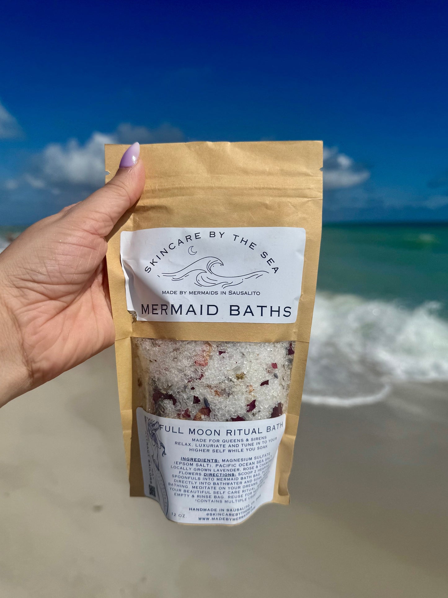 Hand holding a package of Mermaid Baths near the ocean.