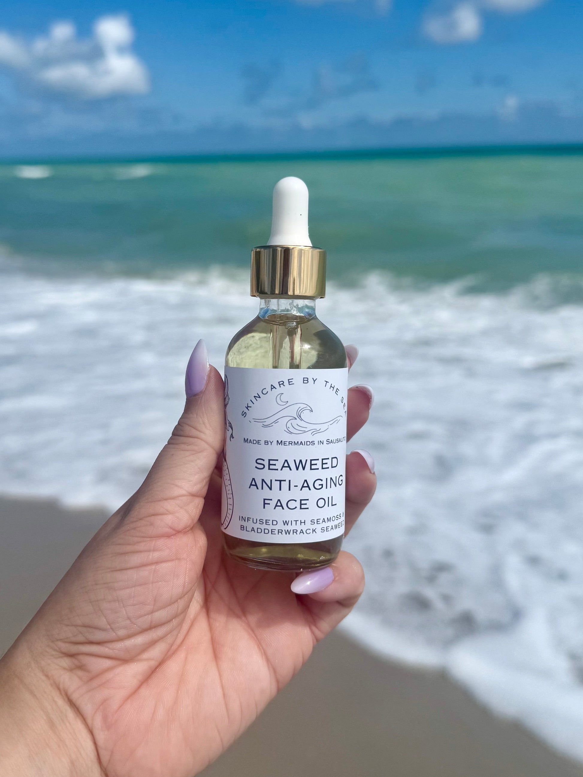Hand holding a bottle of Seaweed Anti-aging face Oil with ocean waves in the background