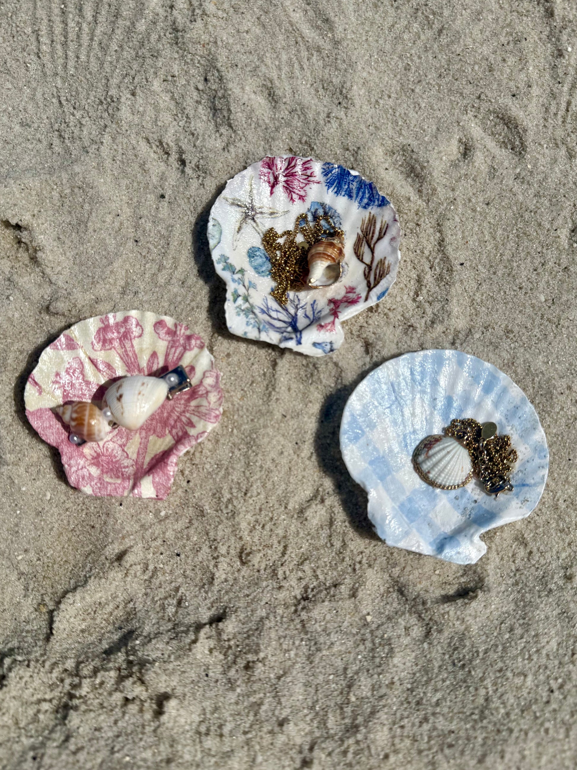 Three colorful seashells with jewelry inside on a sandy surface
