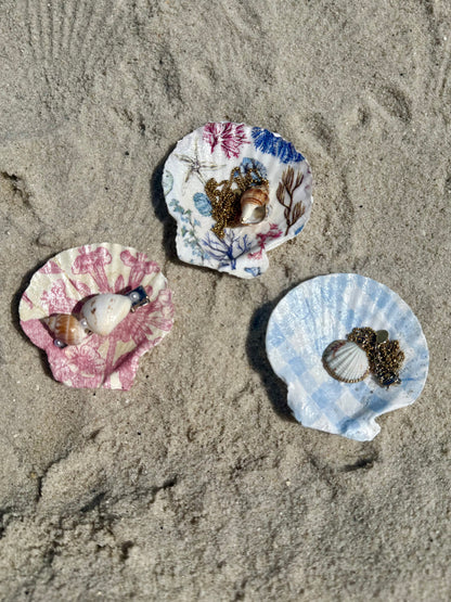 Three colorful seashells with jewelry inside on a sandy surface