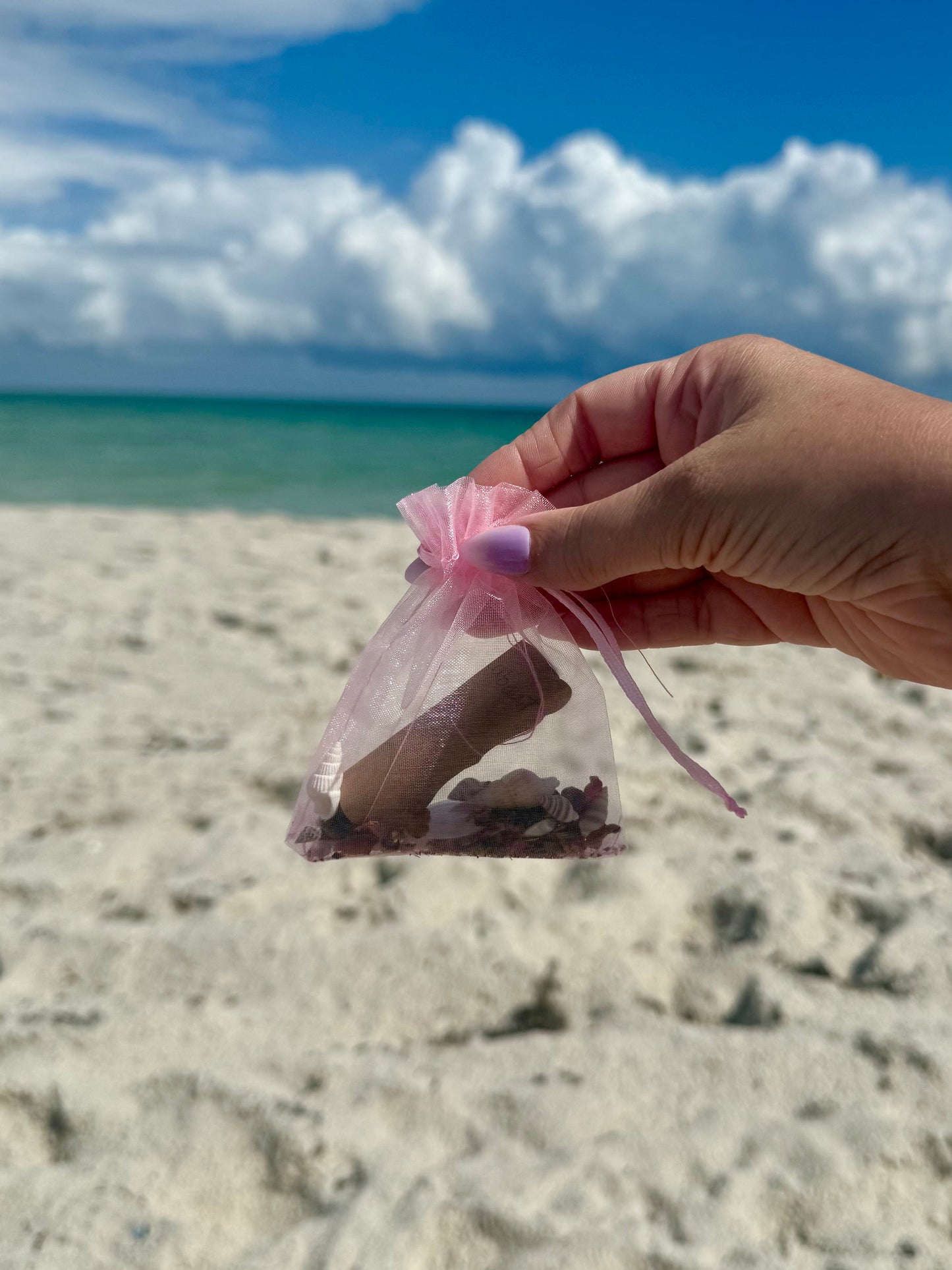 hand holding finished self-love spell pouch with sandy beach sky background